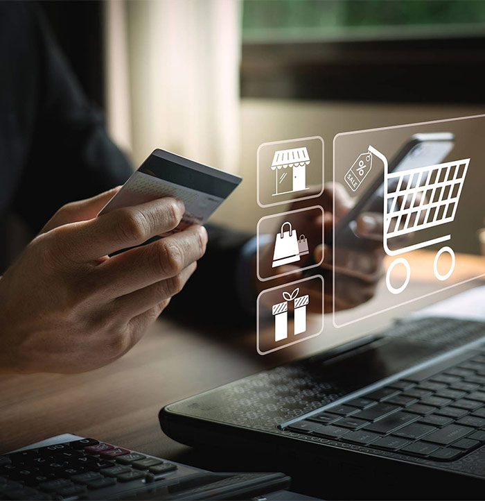 Person holding a credit card near a laptop, with digital shopping icons like a trolley, shop, bag, and gift appearing in the foreground, highlighting the convenience of using e-commerce websites for online shopping.