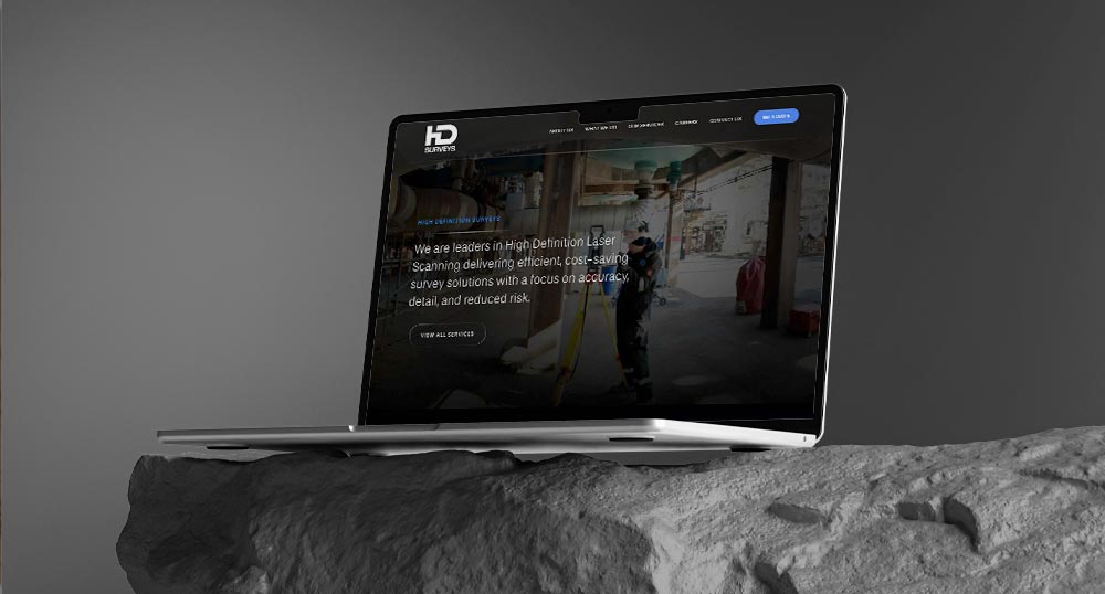 A laptop on a stone surface displays a B2B web design for 3D scanning services, showing a professional working in an industrial environment.